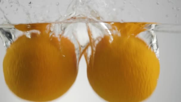 光の背景を背景に水の中にスプラッシュや泡と落ちる2つの新鮮なオレンジ 健康的できれいな食べ物 デトックス ベジタリアン ビーガンフードの概念 ワイドショット — ストック動画