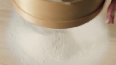 Profesyonel fırıncı elleri, masanın üzerinde siyah arka plana karşı ahşap bir süzgeçten un geçirir. Düşen beyaz parçacıklar. Hamur yoğurma ve lezzetli pizza pişirme kavramı. Üst Manzara. 4K