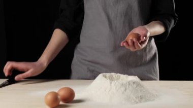 Profesyonel fırıncı bir bıçakla bir yumurta kırar ve yumurtanın içindekileri bir un yığınının içine döker. Hamur yoğurma ve lezzetli pizza pişirme kavramı. Orta atış. 4K