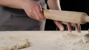 Profesyonel fırıncının elleri ahşap bir masada hamuru yuvarlamak için un ile merdaneyi siliyor. Hamur yoğurma ve lezzetli pizza pişirme kavramı. Kapatın. 4K