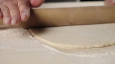 Profesyonel bir fırıncının elleri hamuru un ile ahşap bir masanın üzerinde merdaneyle yuvarlar. Hamur yoğurma ve lezzetli pizza pişirme kavramı. Kapatın. 4K