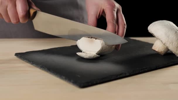 プロのシェフは 黒い背景に黒い板の上に鋭い金属ナイフでキノコをカットします 生地の混練とおいしいピザを調理の概念 閉めろ — ストック動画
