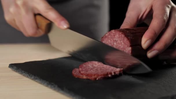 黒を基調とした黒板に鋭い金属のナイフでサラミをカットするプロのシェフ 生地の混練とおいしいピザを調理の概念 閉めろ — ストック動画