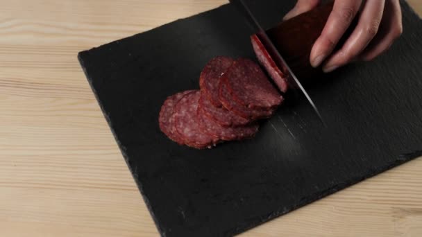 黒を基調とした黒板に鋭い金属のナイフでサラミをカットするプロのシェフ 生地の混練とおいしいピザを調理の概念 最上階だ — ストック動画