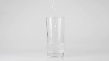 Saf temiz su beyaz zemin üzerinde şeffaf bir bardağa dökülür. Evde kalma ve doğal suyla sağlıklı yiyecekler yeme kavramı. Detoksifikasyon. Orta atış. Yavaş çekim