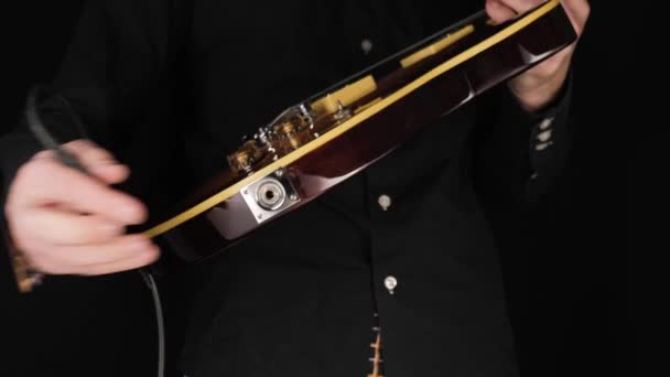 吉他手将乐器电缆插头插入到黑色背景的浅褐色六弦电吉他中 呆在家里 创作一些音乐的概念 自由时间的音响艺术 大范围拍摄 — 图库视频影像