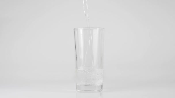 De l'eau fraîche pure est versée dans un verre transparent sur un fond blanc. Concept de rester à la maison et de manger des aliments sains avec de l'eau naturelle. Désintoxication. Au milieu. Mouvement lent 