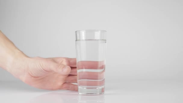 Main prend un verre avec de l'eau pure fraîche de la table blanche sur fond blanc. Concept de rester à la maison et de manger des aliments sains avec de l'eau naturelle. Désintoxication. Au milieu. Mouvement lent 