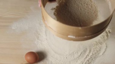 Profesyonel fırıncı elleri, masanın üzerinde siyah arka plana karşı ahşap bir süzgeçten un geçirir. Düşen beyaz parçacıklar. Hamur yoğurma ve lezzetli pizza pişirme kavramı. Ağır çekim. Kapat.