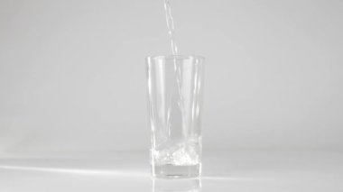 Saf temiz su beyaz zemin üzerinde şeffaf bir bardağa dökülür. Evde kalma ve doğal suyla sağlıklı yiyecekler yeme kavramı. Detoksifikasyon. Orta atış. Yavaş çekim