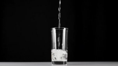 Saf temiz su, siyah zemin üzerinde şeffaf bir bardağa dökülür. Evde kalma ve sağlıklı yiyecekleri doğal suyla yeme kavramı. Detoksifikasyon. Orta atış. Yavaş çekim