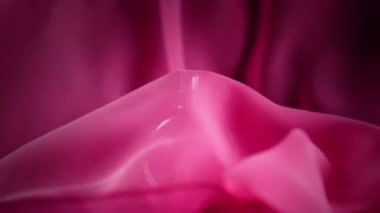 Oval yüzeye çıkan pembe parfüm şişesi ya da gerekli yağlar masanın üstünde, pembe bir bezin altında. Pembe kumaş aniden masadan fırlayıp siyah arka plandaki parfümleri açığa çıkarıyor. Kapat.