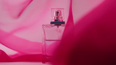 Cyan parfümlü ya da gerekli yağlı düz yüzey şişesi beyaz masada. Pembe kumaş dalgalanır ve şişenin etrafında dalgalanır. Aroma ve koku kavramı. Kapatın. Yavaş çekim