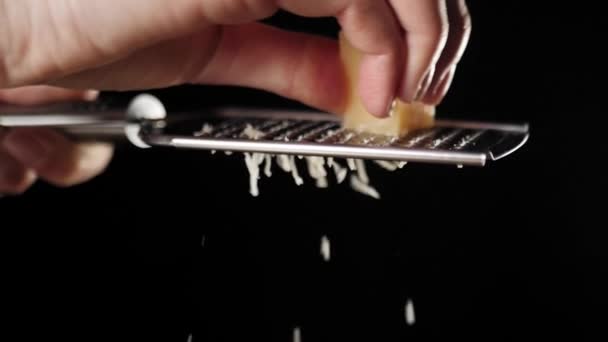 专业厨师在烤架上擦意大利芝士 烤奶酪落在比萨饼上 配上意大利腊肠和黑色背景 做美味披萨的概念慢动作靠近点 — 图库视频影像