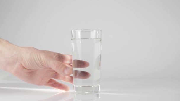 Main prend un verre avec de l'eau pure fraîche de la table blanche sur fond blanc. Concept de rester à la maison et de manger des aliments sains avec de l'eau naturelle. Désintoxication. Au milieu. Mouvement lent 