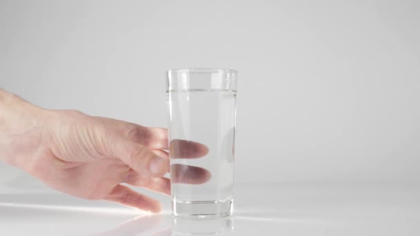 手は白い背景に白いテーブルから純粋な新鮮な水でガラスを取ります 家にいて 自然の水で健康的な食べ物を食べるという概念 解毒剤だ 撃たれた スローモーション — ストック動画