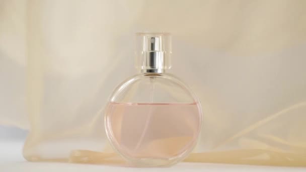 ピンクの香水やエッセンシャルオイルと楕円形の表面ボトルは 白いテーブルの上にあります 周囲にベージュの生地が浮かび ボトルの周りの空気中の波 香りと香りの概念 閉めろ スローモーション — ストック動画