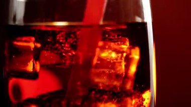 El kırmızı bir pipet kullanarak buz küplerini kolayla karıştırır. Siyah arka planda kahverengi röfleli bir bardak sodanın içinde baloncuklu buz yüzüyor. Kola ya da soda içme kavramı. Kapatın. 4K