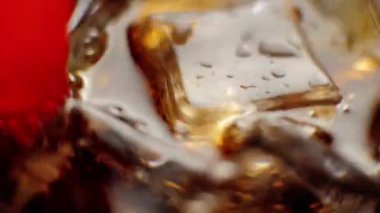 El kırmızı bir pipet kullanarak buz küplerini kolayla karıştırır. Siyah arka planda kahverengi röfleli bir bardak sodanın içinde baloncuklu buz yüzüyor. Kola ya da soda içme kavramı. Kapatın. Üst Manzara. 4K