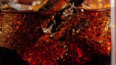 Kamera, siyah arkaplana karşı siyah saman ve kahverengi röfleli bir bardak kolayla buz küplerinden yukarıya doğru hareket ediyor. Kola ya da gazoz içmek, rahatlamak ve eğlenmek. Kapatın. 4K