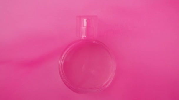 ピンクの香水やエッセンシャルオイルと楕円形の表面ボトルはピンクの布の下に白いテーブルの上にあります ピンクの布の波は 突然離れてテーブルの香水を公開からなびかせます 閉めろ スローモーション — ストック動画