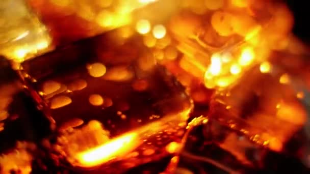 Les glaçons flottent et tournent avec des bulles dans un verre de cola aux reflets bruns sur fond noir. Concept de boire de la coke ou du soda, se détendre et s'amuser à la maison. Ferme là. Vue de dessus. 4K 