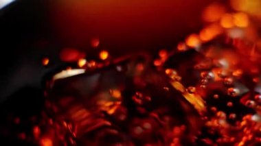 Buz küpleri siyah arka planda kahverengi röfleli bir bardak kolada kabarcıklarla yüzer ve döner. Kola ya da gazoz içmek, evde rahatlamak ve eğlenmek. Kapatın. Üst Manzara. 4K