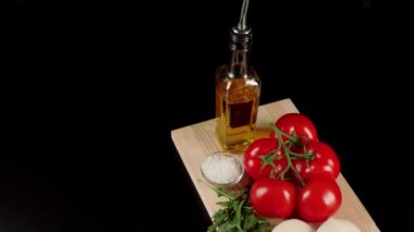 Modern Caprese salatası. Bir dalda taze sulu kırmızı domatesler, mozzarella peyniri, roka yaprakları, zeytinyağı ve deniz tuzu siyah arka planda tahtada. Kamera aşağı kayıyor. Üst görünüm