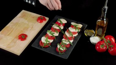 Profesyonel şef tuzları hazır caprese salatası. Taze domateslere deniz tuzu damlaları, mozzarella peyniri ve roka yaprakları zeytinyağı şişesinin yanındaki kara tahtada. Orta atış. Üst görünüm