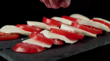 Profesyonel şef tuzları hazır caprese salatası. Taze domateslere deniz tuzu damlaları ve kara tahtada mozzarella peyniri. Yan görüş. Kapat.