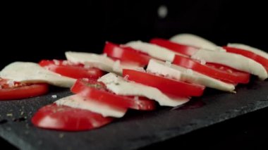 Profesyonel şef, hazır Caprese salatası ve Akdeniz bitkisi serpiyor. Taze domateslere taze otlar ve kara tahtaya mozzarella peyniri dökülür. Yan görüş. Kapatın. 4K