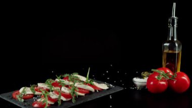 Kamera hazır Caprese salatasına bakıyor. Taze sulu domatesler, mozzarella peyniri ve kara tahtada akdeniz otları ve deniz tuzu bulunan roka yaprakları. Orta atış. 4K