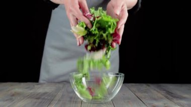 Profesyonel aşçı, taze sulu yeşil ve ahşap masaya boş cam kaseye kestane rengi marul döker. Salatadan, kiraz domatesinden, salatalıktan ve soğandan taze yaz salatası yapma fikri. 4K