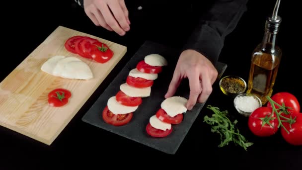 プロのシェフが料理のプレゼンテーションを行い ブラックボード上の新鮮なジューシーなトマトとモッツァレラチーズを含むカプレーゼサラダの成分をレイアウトします 撃たれた 最上階だ — ストック動画