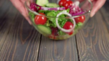 Profesyonel aşçı masaya zeytinyağı ve deniz tuzu ile taze salata, soğan, salatalık ve kiraz domatesinden oluşan cam bir kâse koyar. Üst Manzara. 4K