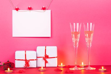 Sevgililer Günü kartında kalpler, hediyeler, güller, mumlar ve pembe arka planda iki kadeh şampanya. San Valentin ve Aşk konsepti.