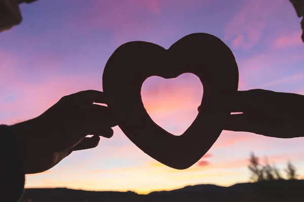 Σιλουέτα δύο χεριών που κρατούν μια καρδιά το ηλιοβασίλεμα. Έννοια της αγάπης και της σχέσης — Φωτογραφία Αρχείου