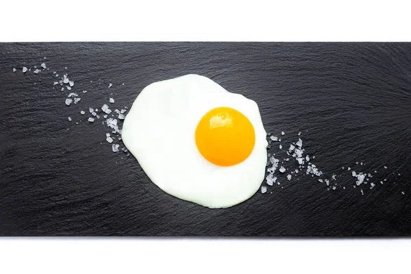 Huevo frito en plato de pizarra con sal sobre fondo blanco. Concepto de cocina y comida . — Foto de Stock