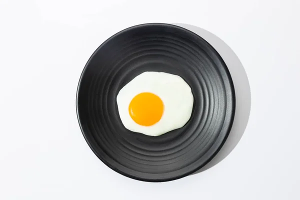 Huevo frito en plato negro sobre fondo blanco. Concepto de cocina y comida . — Foto de Stock