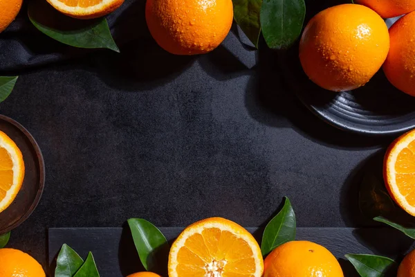 Fond avec des oranges, des tranches d'orange et des feuilles d'orange sur fond texturé noir — Photo