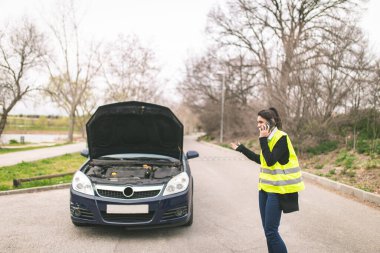 Arabası yolda bozulmuşken cep telefonuyla konuşan beyaz bir kadın. Otomobil ve Yol Yardımı Konsepti..