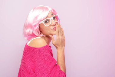 Pembe peruklu ve kazaklı, beyaz gözlüklü, fotoğraf stüdyosunda tuhaf poz veren beyaz bir kadın. Komik anlamlı kadınlar ve renkli portre konsepti. Pembe..