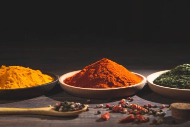 Ahşap masada çeşitli renkli otlar ve baharatlar. Kopyalama alanı olan karanlık bir arkaplan. Yemek malzemeleri ve baharat konsepti.