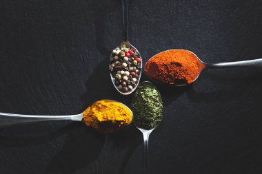 Biberli kaşıklar, biber, maydanoz ve siyah arka planda zerdeçal, fotokopi alanı, üst manzara. Yemek malzemeleri ve baharat konsepti.