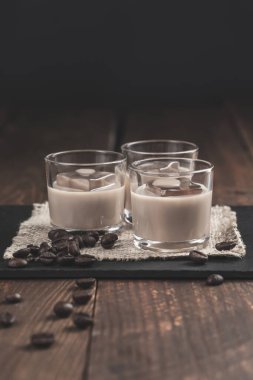Buzlu kremalı kahve likörü ve ahşap arka planda kahve çekirdekleri..