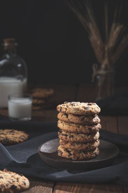 Çukulatalı bisküviler, bir bardak ve bir şişe sütle ahşap bir zeminde, koyu arka planda. Tatlı yemek konsepti.