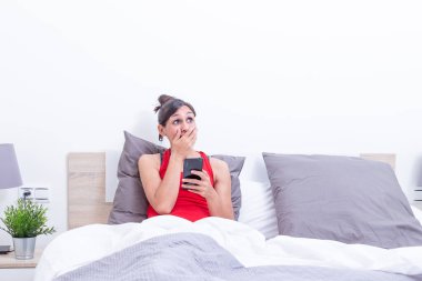 Yataktaki mutlu genç kadın elinde cep telefonuyla şaşırmış görünüyor..