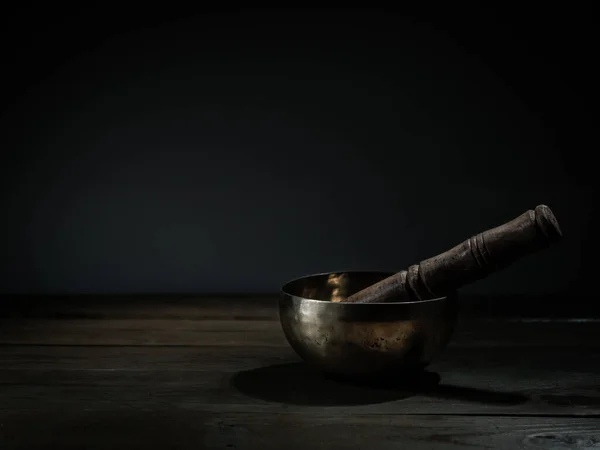 old Tibetan singing bowl on wooden base, black background. Music therapy.