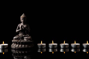 Meditasyonda oturan Buda heykeli, siyah fotokopi alanı olan mum hattı. Zen ve meditasyon kavramı.