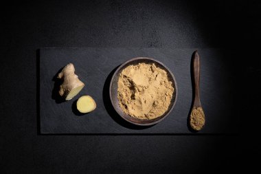 Zencefil ve zencefil tozu parçaları, tahta kaşık ve tabakta, siyah arka planda. Üst Manzara. Doğal gıda konsepti.